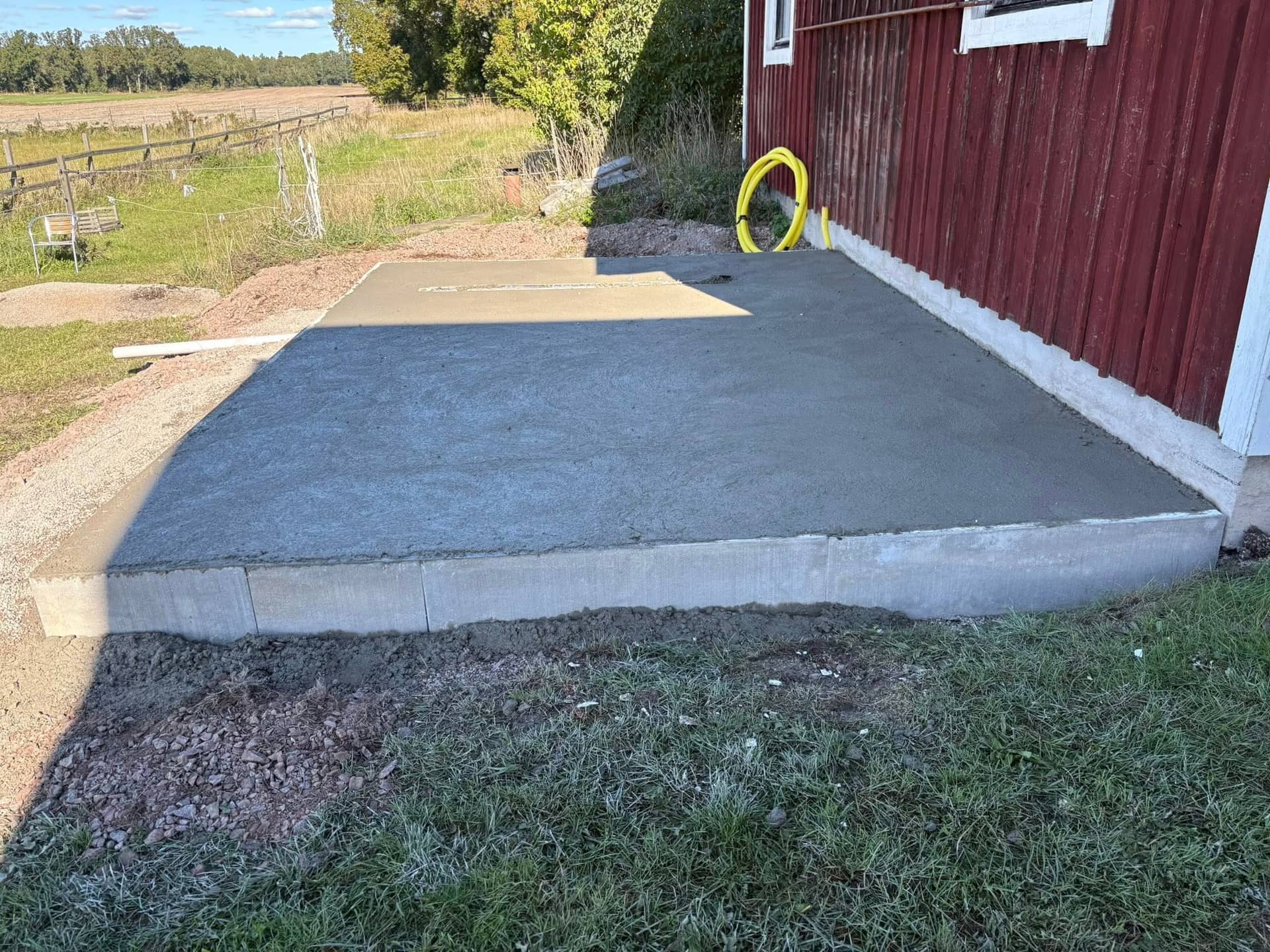 Nygjuten betongplatta vid röd träfasad